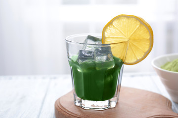 Glass of wheat grass juice with lemon on wooden table