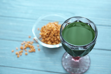 Glass of wheat grass juice and seeds on wooden table