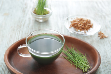 Plate with cup of wheat grass juice on table