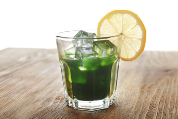 Glass of wheat grass juice with lemon on wooden table