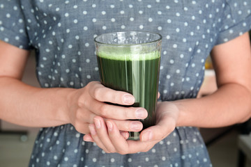 Woman holding glass of wheat grass juice, close up