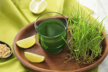 Plate with glass of wheat grass juice on table