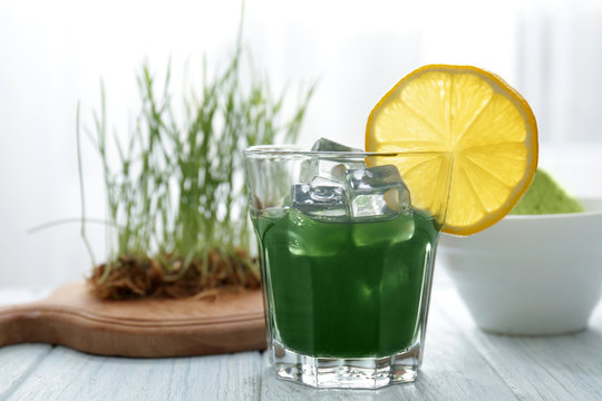 Glass of wheat grass juice with lemon on wooden table