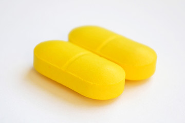 two yellow pills on white background