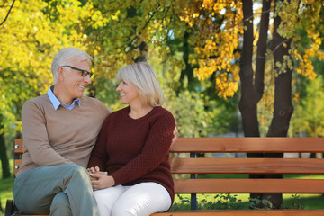 Cute elderly couple sitting on bench in autumn park