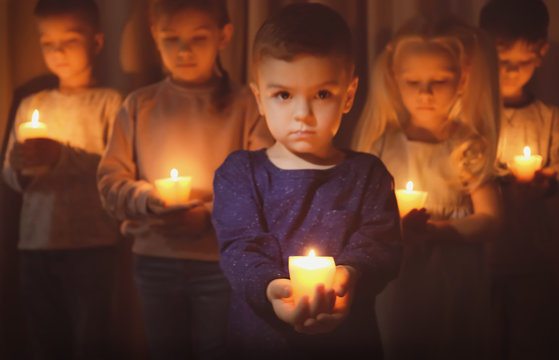 Little children holding burning candles in darkness