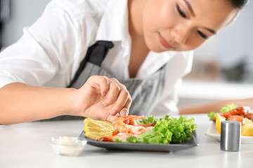 Beautiful Asian woman preparing dish with shrimps at table in kitchen