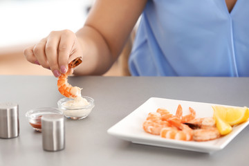 Obraz na płótnie Canvas Young woman eating shrimps at table