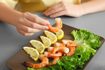 Woman holding tasty shrimp over plate on table