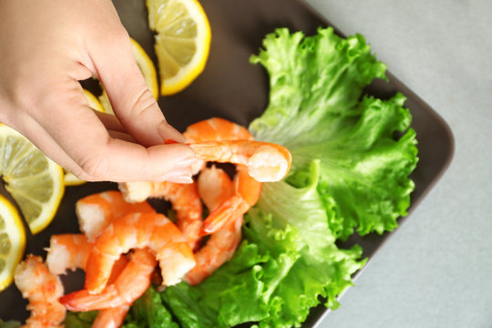 Woman holding tasty shrimp over plate on table