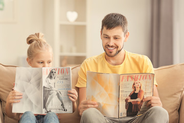 Cute little girl and her father reading magazines at home