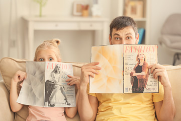 Funny little girl and her father with magazines at home