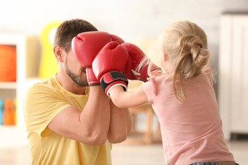 Cute girl and her father in boxing gloves playing at home