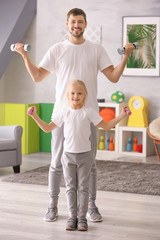 Cute girl and her father training with dumbbells at home