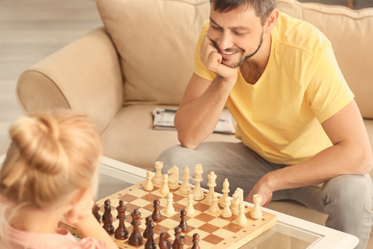 Cute girl playing chess with her father at home
