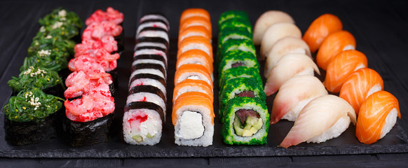 Tasty appetizing multicolored sushi rolls set with wide assortment of fillings, served on black stone slate. Restaurant menu