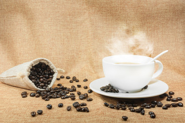 Cup of fresh coffee with coffee beans on burlap warm cup on brown background with free space for text