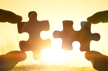 two hands trying to connect couple puzzle piece with sunset background. Jigsaw alone wooden puzzle...