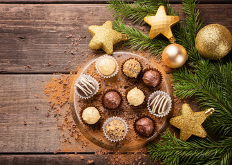 Fototapeta na wymiar Chocolate candy from chocolate of various kinds on a metal stand on a wooden background. Spruce branches and New Year toys lie side by side. Christmas concept. Copy space.