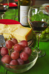 Close up still natural hand made cheese with wine in the glass and bottle also grape on the green wood table