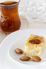 Piece Basbousa Traditional Arabic Semolina Cake with Nuts Orange Blossom Water and glass of tea. Selective focus.
