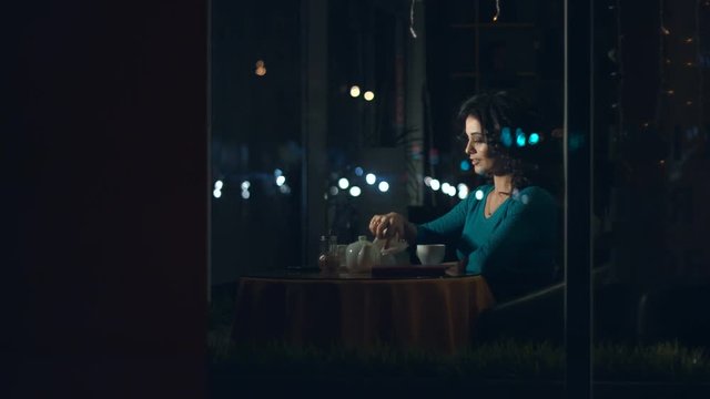Cute womanin in a cafe.
Slow motion. A pretty woman is sitting in a cafe behind the glass and dreams.
She looks at the paper boat. The glass reflects the traffic of urban transport.