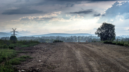 Fototapeta premium Rural mountain country road at misty summer morning with dramatic clouds and power lines