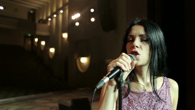 Closeup portrait of a beautiful singer with a microphone. Young woman singing in microphone on an empty stage, close-up.