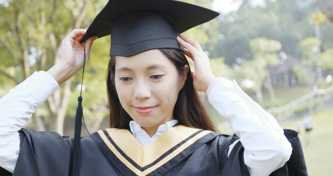 Woman adjusting her graduation gown and mortarboard in campus