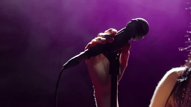 Microphone in hand singer on stage. Close-up. Silhouette of singer on stage with microphone in hand. Dark background, smoke, spotlights.