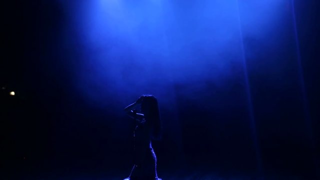 A beautiful singer poses on stage in the dark under the light of a blue spotlight.