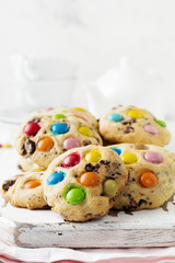 Stack of children's cookies with colorful chocolate candies in a sugar glaze on a white light wooden background. Selective focus