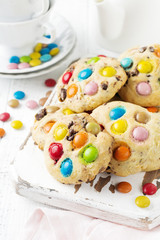Stack of children's cookies with colorful chocolate candies in a sugar glaze on a white light wooden background. Selective focus