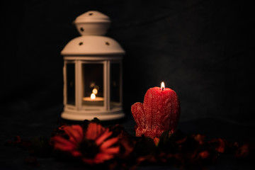 Still-life on a dark background. Decor of candles and candlesticks, with daisies and red leaves. Selective focus.