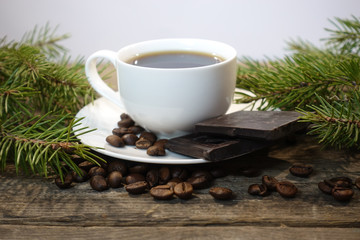 A cup of coffee with spruce branches, coffee beans and a piece of chocolate.