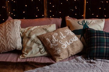 christmas coziness evening, pillows on a couch with garland light bokeh background. Let it snow text on pillow