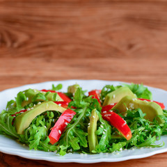 Home healthy salad for lunch or dinner. Raw avocado, arugula, red pepper and sesame seeds salad on a white plate. Raw vegan meal. Closeup