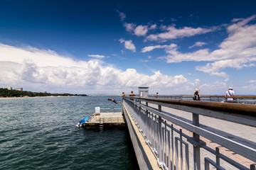 Obraz premium boy jumped from bridge to water. summer fun in hot weather. jump in water.. crystal clear seawater and child jumps into the water against a blue sky with beautiful white clouds.