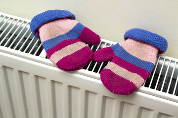 Children's warm hand knitted striped woolen gloves drying on hea