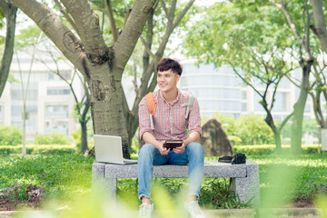 Attractive male asian student is using computer in university's park