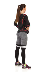 Young Woman Standing Legs Apart In Fitness Outfit. Rear Side View.