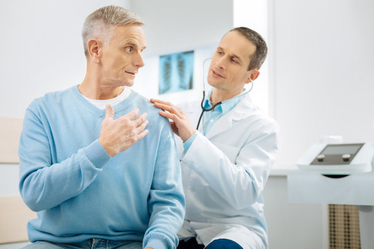 Professional osteopath. Smart handsome male doctor sitting behind his patient and wearing stethoscope while examining him