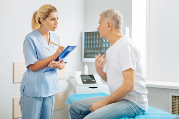 Obraz premium Personal therapist. Nice good looking elderly man sitting in the doctors office and speaking to his therapist while complaining about his pain