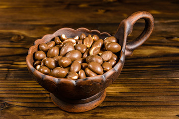 Peanuts with chocolate glaze in a ceramic bowl on wooden table