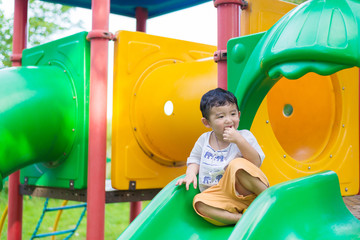 Little Asian kid playing slide at the playground under the sunlight in summer, shallow DOF