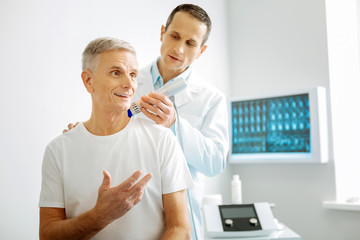 Ultrasound check. Smart nice handsome doctor standing behind his patient and using special scanning device while doing a checkup