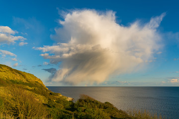 Fototapeta na wymiar Single Raincloud with a little bit of a rainbow at Osmington Bay, near Weymouth, Jurassic Coast, Dorset, UK