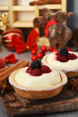 Christmas dessert concept. Delicious panna cotta tarts with fresh blackberry and raspberry on vintage wooden tray. Holiday background.