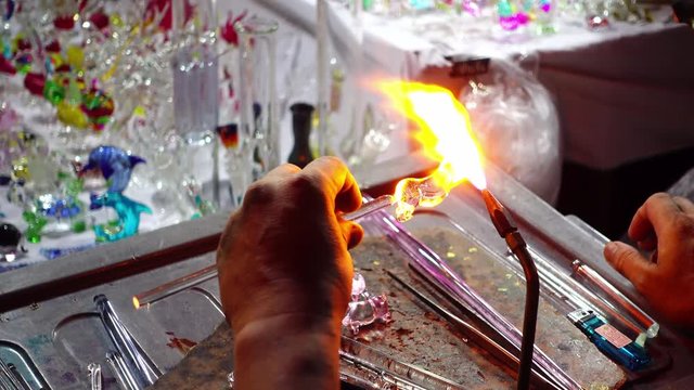 Close up handicrafts glass maker making a glass subject by melting glass with a flaming torch from blowtorch on new glass art piece.
