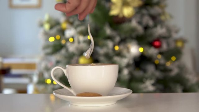 Man's hand stirs christmas coffee, New Year tree on background